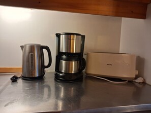 A kitchen counter with a stainless steel kettle, a coffee maker, and a white toaster.