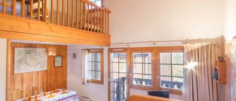 A wooden interior with a dining table set, a bench, and a view of the outside through large windows.