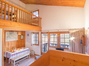 A wooden interior with a dining table set, a bench, and a view of the outside through large windows.