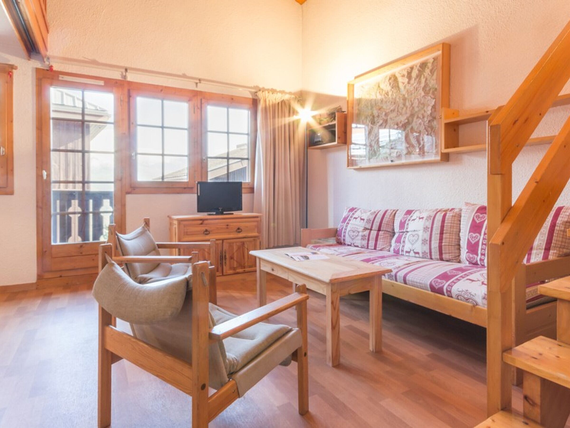 A cozy room with a wooden sofa, a wooden chair, a small table, and a TV on a wooden cabinet.