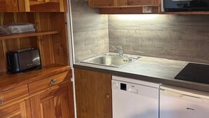 Een compacte keuken met houten kastjes, een inbouwvaatwasser en een roestvrijstalen spoelbak.