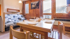 Een gezellige kamer met een houten eettafel gedekt voor twee personen, een bank met een gebloemd plaid en een groot raam met uitzicht op de bergen.