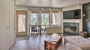 Ein modernes Wohnzimmer mit Kamin, einem Essbereich mit Tisch und Stühlen sowie großen Fenstern mit Vorhängen.