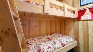 Camera con letto a castello in legno, un letto inferiore e un materasso con motivo rosso e bianco.