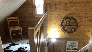 Un intérieur en bois avec une chaise en bois, une horloge, une porte et un tapis en peau de vache.
