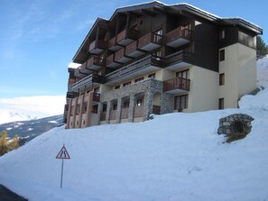 A multi-story hotel with balconies, stone facade, and a snow-covered slope.