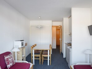 Una habitación compacta con una mesa de comedor, sillas, microondas, televisor y una cama con cubre color rojo.