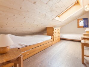 A small, wooden-paneled attic bedroom with a single bed, a wooden dresser, and a desk.