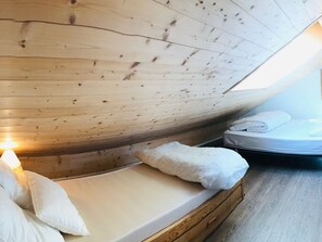 Een houten plafond met schuine constructie, een bed met wit beddengoed en een nachtkastje met een lamp.