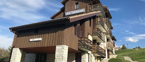 A multi-story wooden building with a stone base, balconies, and a sign reading "LES CHOUCAS."