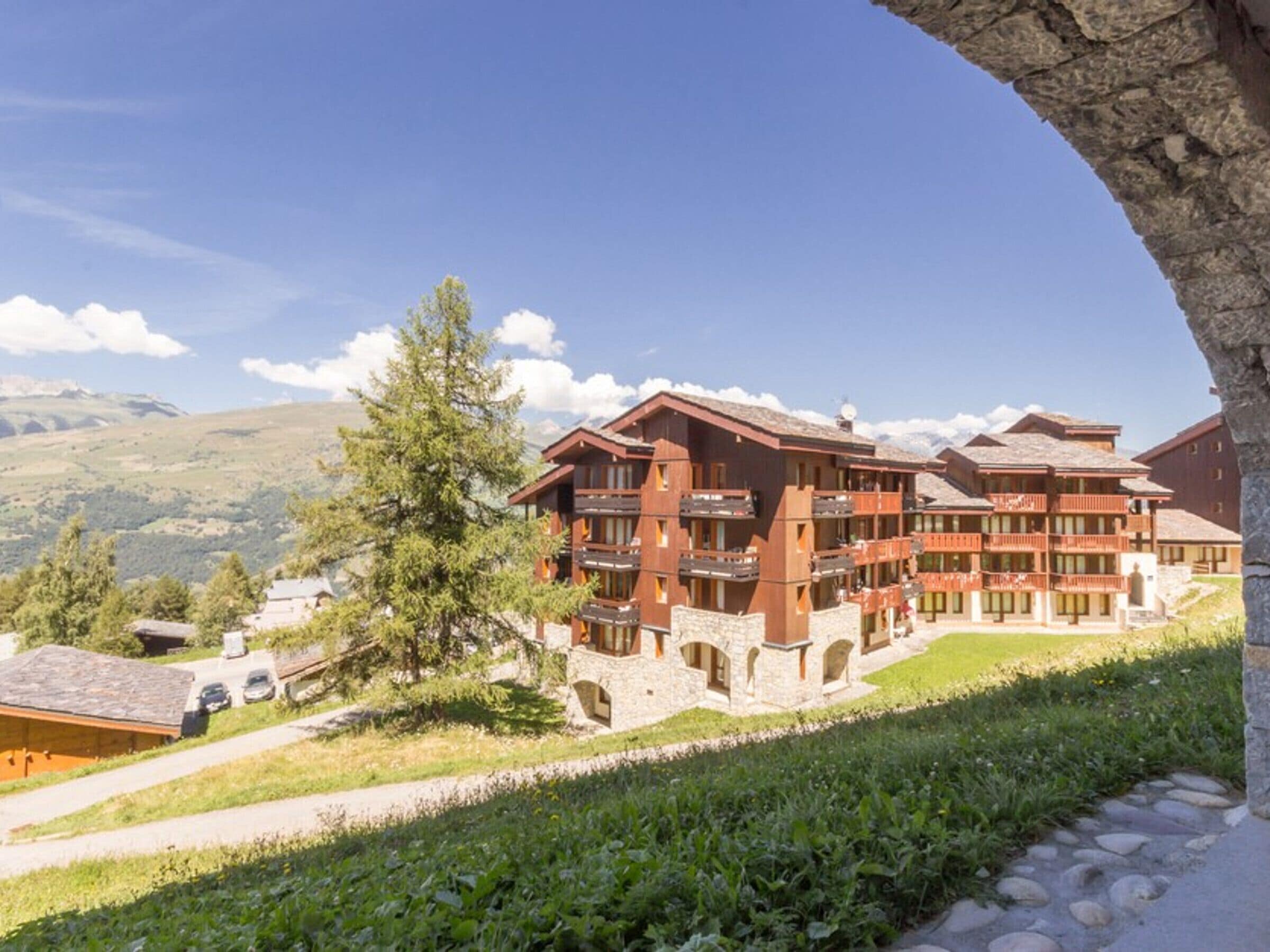 A multi-story lodge with balconies, set against a mountainous backdrop.