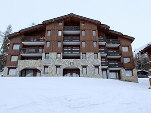 A multi-story hotel with stone and wood exterior, balconies, and a snowy landscape.