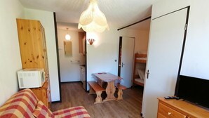 A cozy room with a checkered bed, a wooden dresser, a television, and a kitchenette in the background.