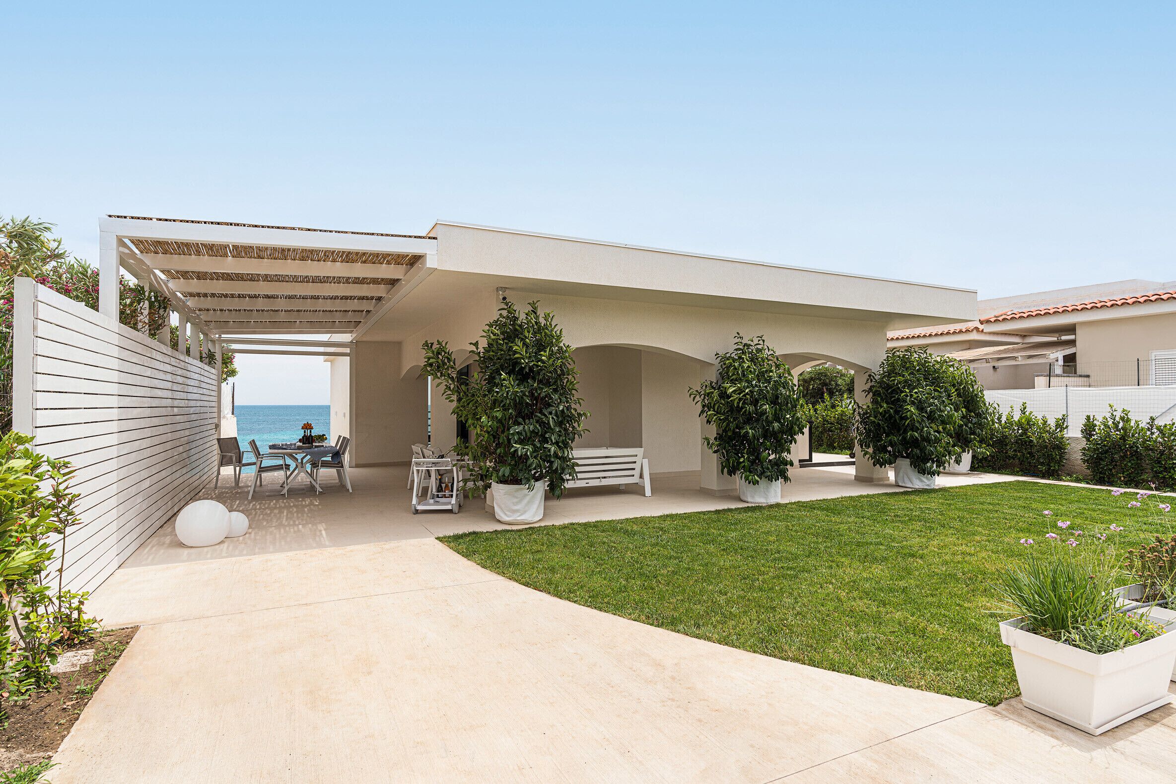 A modern house with a covered patio, a lawn, and potted plants.