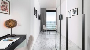 Una moderna camera d'albergo con pavimento in marmo, una scrivania con lampada, una sedia e vista mare attraverso un'ampia finestra.