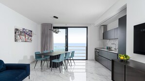 Una cucina moderna con una grande finestra, una zona pranzo con tavolo e sedie, e un soggiorno con divano.