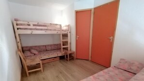 Une chambre avec un lit superposé, un petit bureau, une armoire et un lit.
