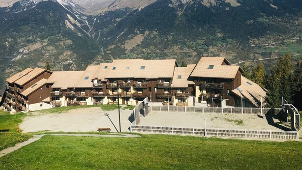 Un hôtel de style chalet, composé de plusieurs bâtiments en bois, avec une cour centrale et un paysage montagneux en toile de fond.