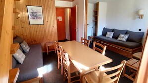 Une pièce chaleureuse avec un plafond en bois, une table à manger avec des chaises, un canapé avec des coussins et un petit meuble en bois.