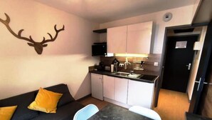 Ein kompakter Wohnraum mit Küchenzeile, einem Sofa mit gelben Kissen und einer an der Wand befestigten Dekoration aus Hirschgeweihen.