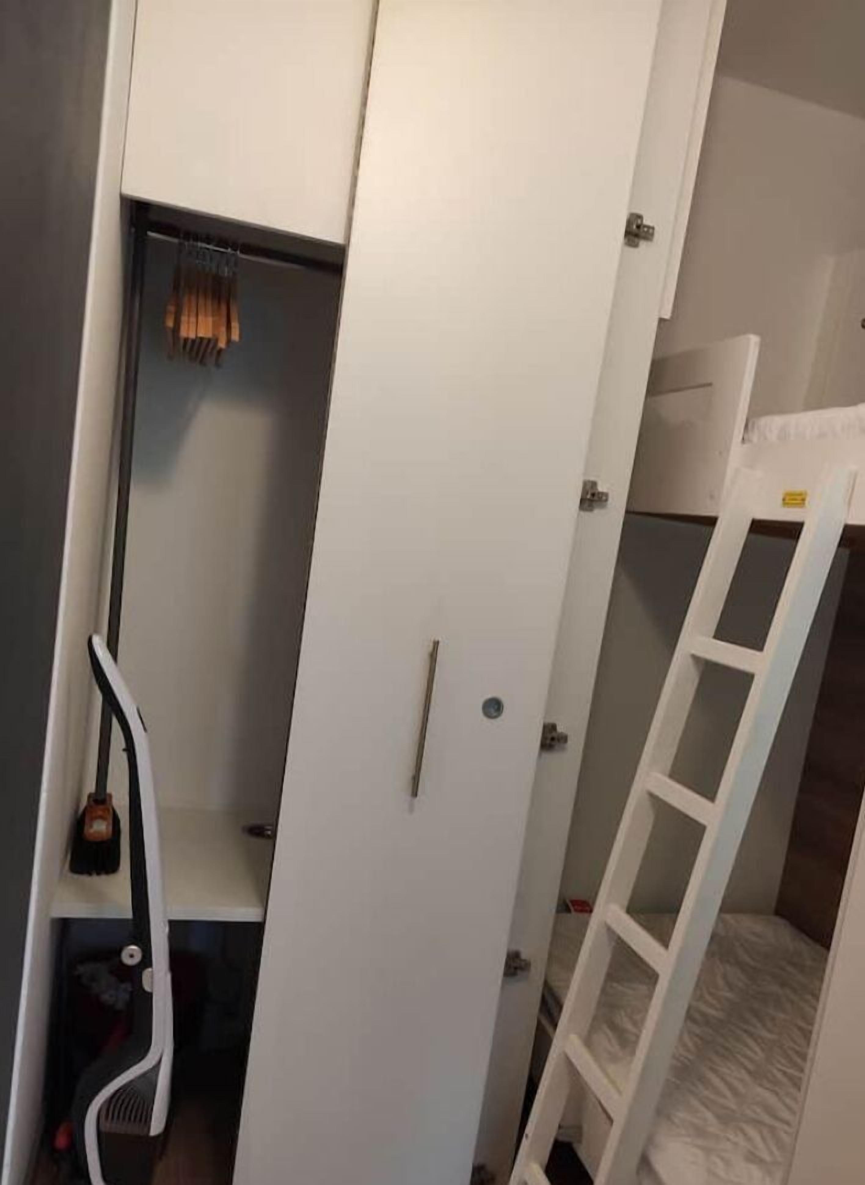 Una habitación con una cama litera, un armario blanco y una pequeña escalera.