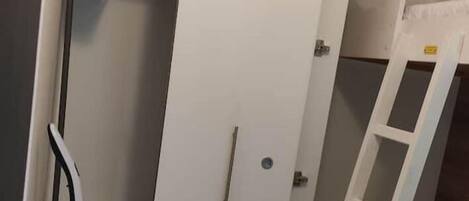 Una habitación con una cama litera, un armario blanco y una pequeña escalera.
