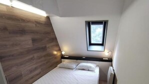 Ein kleines, modernes Schlafzimmer mit Holzbalkendecke, einem Einzelbett, einem kleinen Fenster und einer fest installierten Heizung.