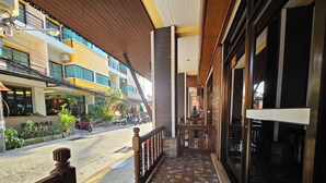 A covered outdoor area with a tiled floor, a wooden railing, and a view of the street with parked motorcycles. - Nanai 2 Residence Patong (Patong)