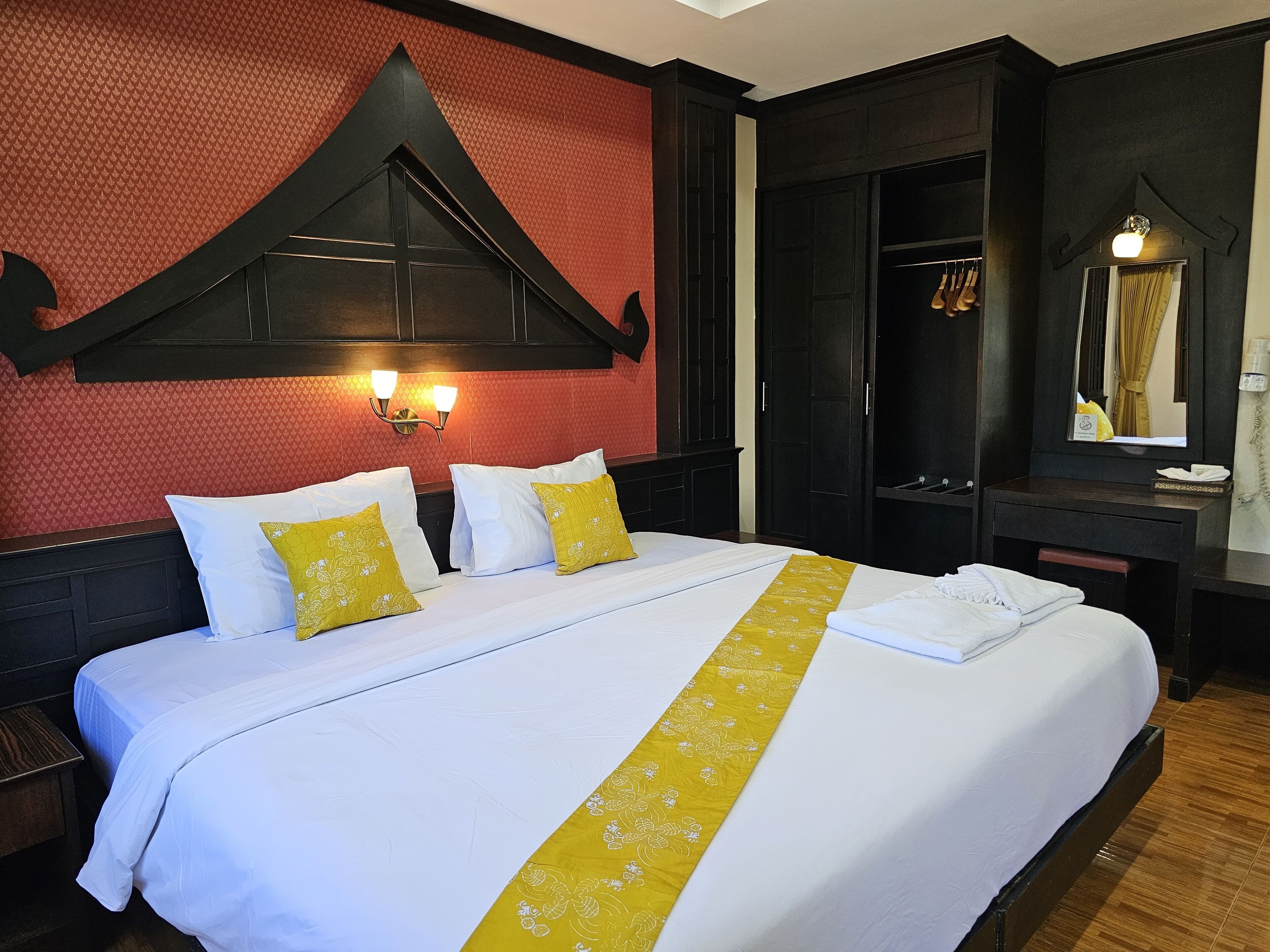 A hotel room with a large bed, two bedside tables, a wardrobe, a mirror, and a wall-mounted light fixture.