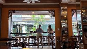 A restaurant with a ceiling fan, wooden furniture, and a view of the street outside. - Nanai 2 Residence Patong (Patong)