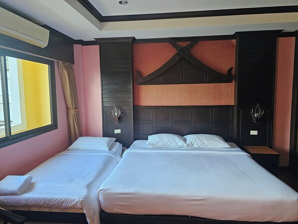 A hotel room with two single beds, a window with curtains, a decorative wall panel, and a ceiling vent.