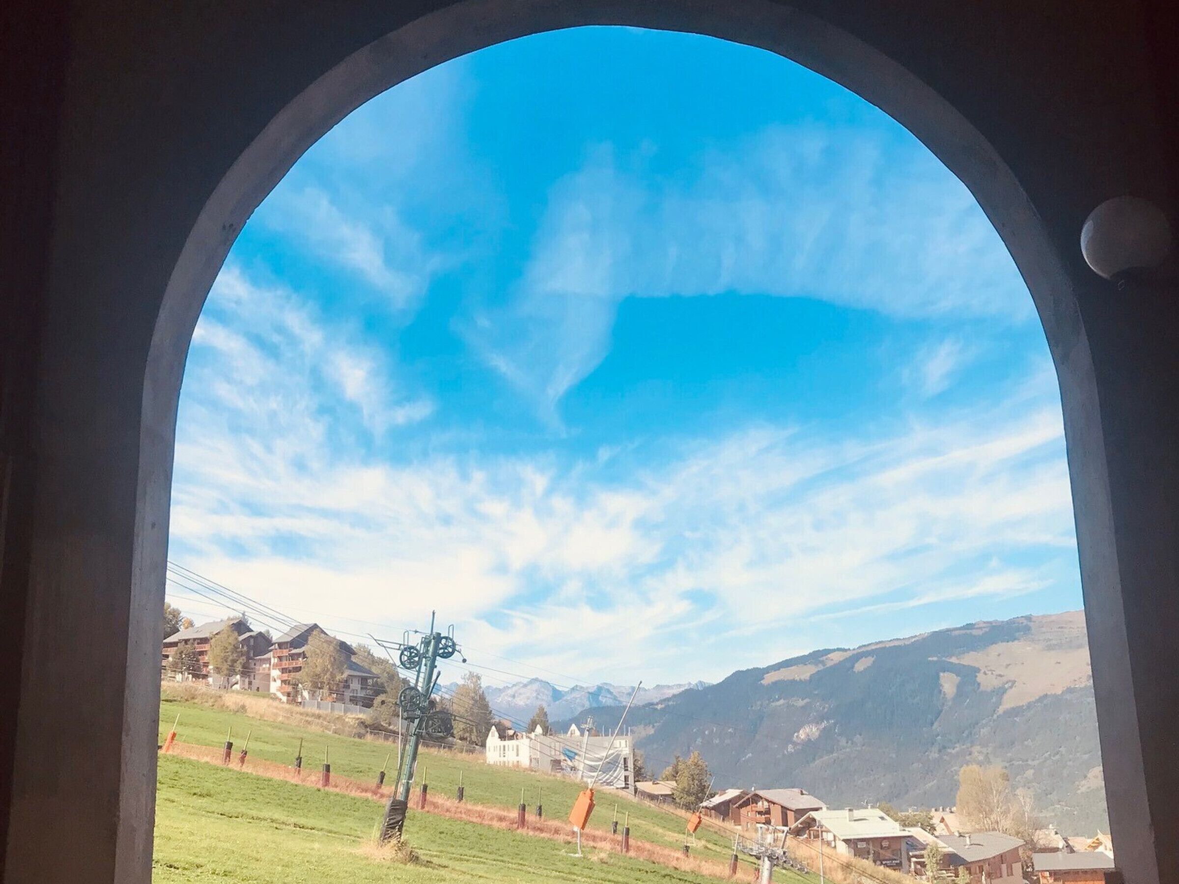 A view through an arched window of a mountainous landscape with houses and a power line structure.