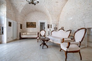 A room with a stone ceiling, a white sofa, a wooden chair, and a small round table.