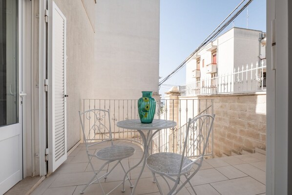 A balcony with a table and chairs, a green vase, and a white door.