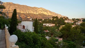 A coastal town with a prominent mountain in the background, a white building with a red door, and lush greenery. - Luxurious 3 bedroom villa with stunning panoramic views in Denia (Denia)