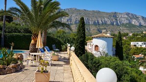 A terrace with outdoor seating, a palm tree, and a mountain backdrop. - Luxurious 3 bedroom villa with stunning panoramic views in Denia (Denia)