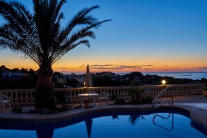 A pool area with a palm tree, lounge chairs, and a view of the sunset over the ocean. - Luxurious 3 bedroom villa with stunning panoramic views in Denia (Denia)