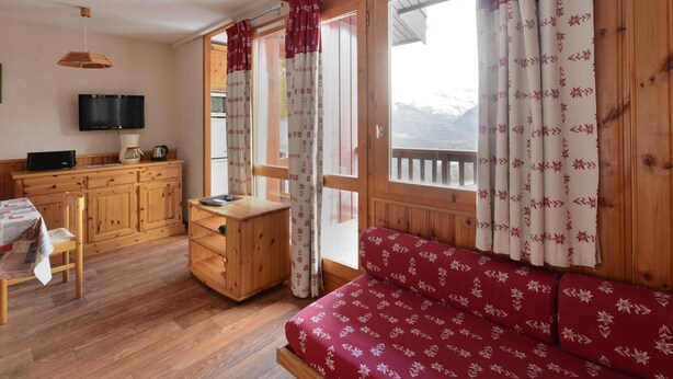 Une pièce confortable, meublée en bois, avec un téléviseur et un canapé agrémenté de rideaux à motifs floraux.