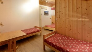 Une pièce comprenant deux lits superposés en bois, une table en bois et une porte donnant sur une autre pièce.