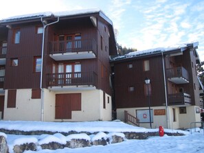 Un edificio de varios pisos con balcones, un letrero de tienda de esquí y suelo cubierto de nieve.