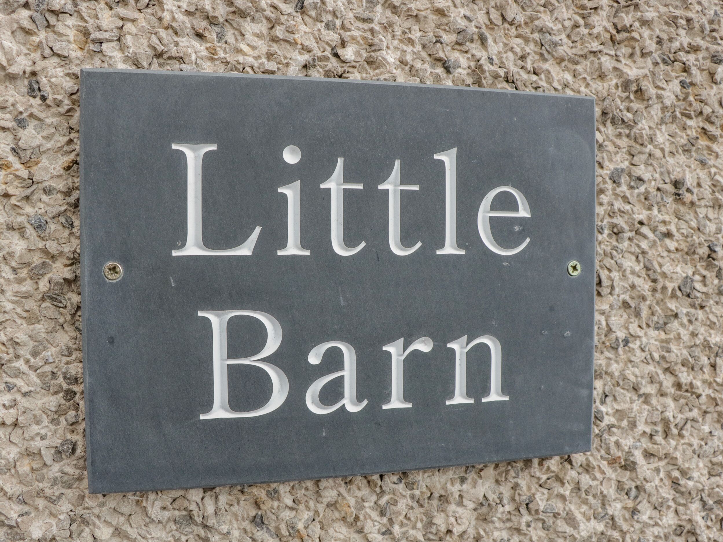 Uma placa de ardósia com a inscrição 'Little Barn' fixada numa parede texturizada.