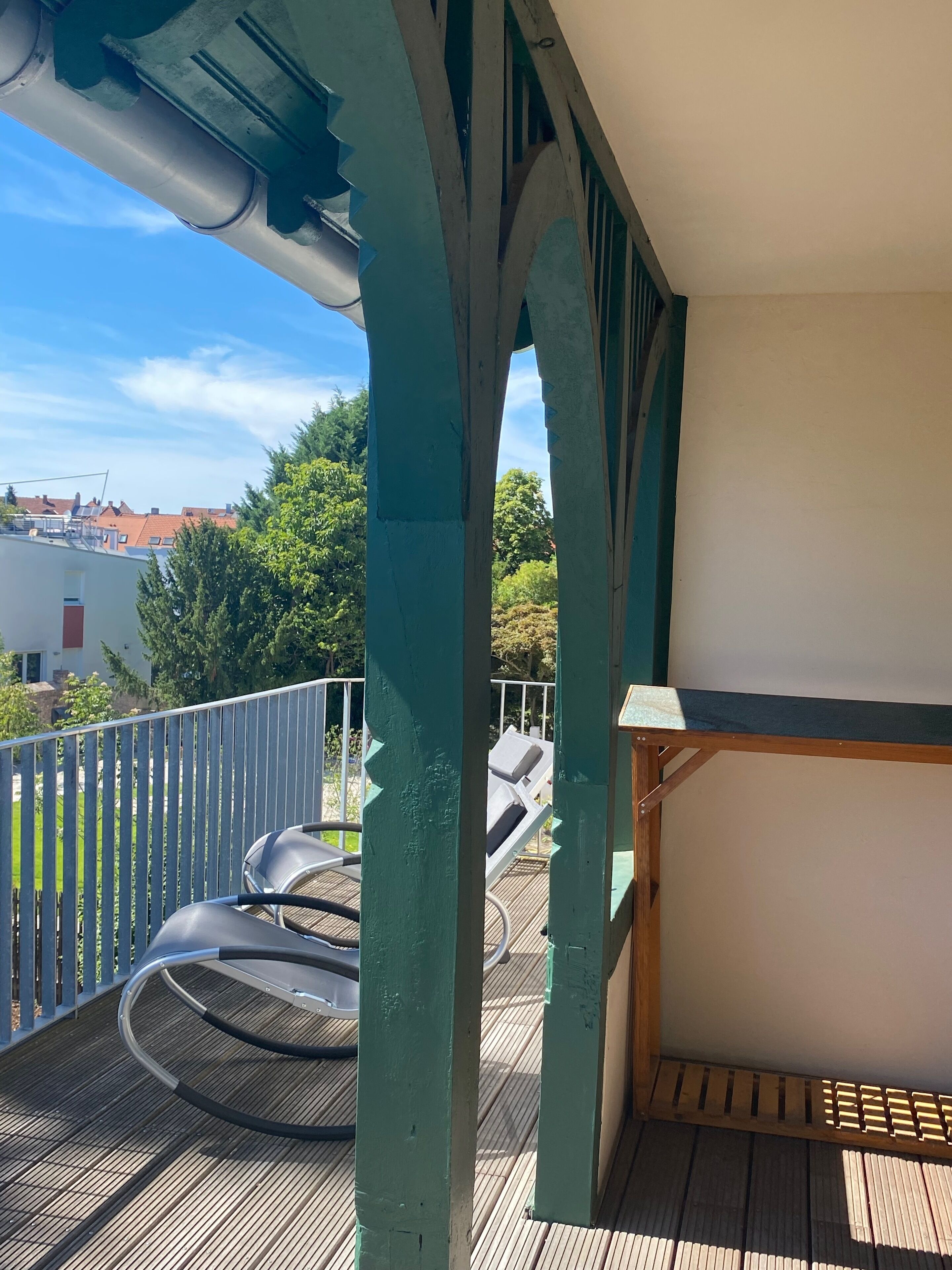 Varanda com vista para uma área residencial, deck de madeira e guarda-corpo de metal.