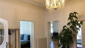 En rummelig stue med trægulv, radiator, en potteplante og en lysekrone.