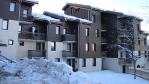 Un edificio residencial de varios pisos con balcones, suelo cubierto de nieve y cielo despejado.