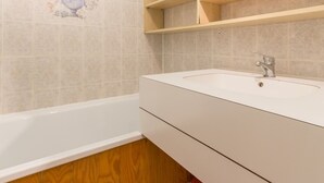 Un baño con una bañera, un lavabo blanco y armarios de madera.