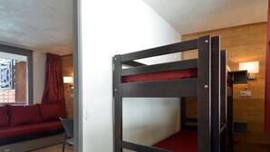 A bunk bed with red bedding, a sofa with red cushions, a chair, and a wall-mounted TV. - Renovated and Comfortable Studio · Heart of Resort (Plagne Bellecôte)