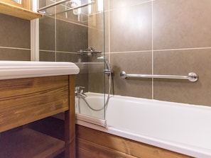 Un bagno con un mobile bagno in legno, cabina doccia in vetro e maniglia di sostegno.