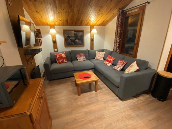 Un accogliente soggiorno con un divano modulare grigio, pavimento in legno e soffitto in legno.