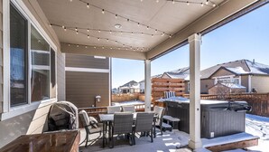 Een overdekt terras met tuinmeubilair, een jacuzzi en uitzicht op omliggende huizen.