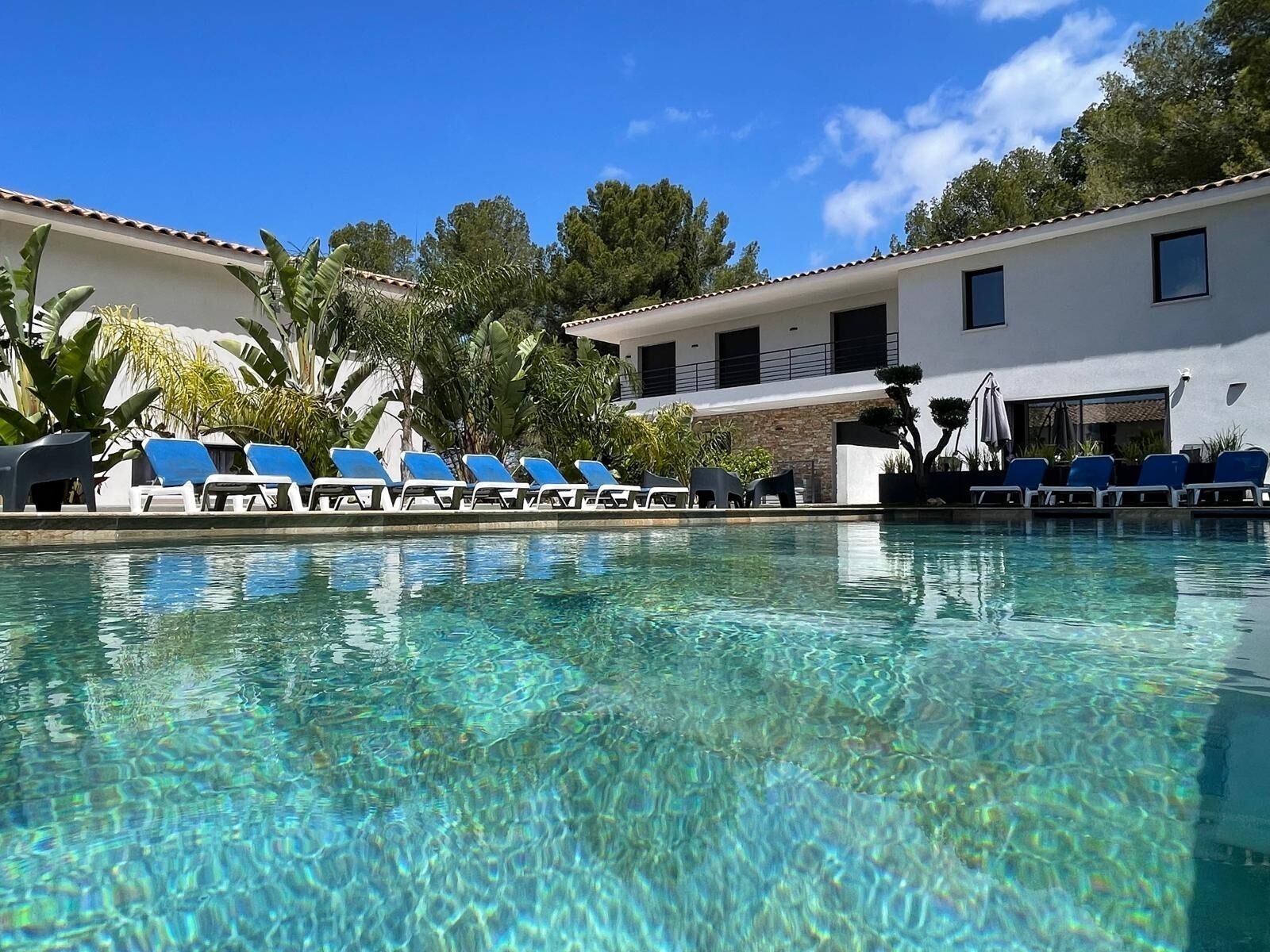 A clear swimming pool with blue lounge chairs arranged along the edge.